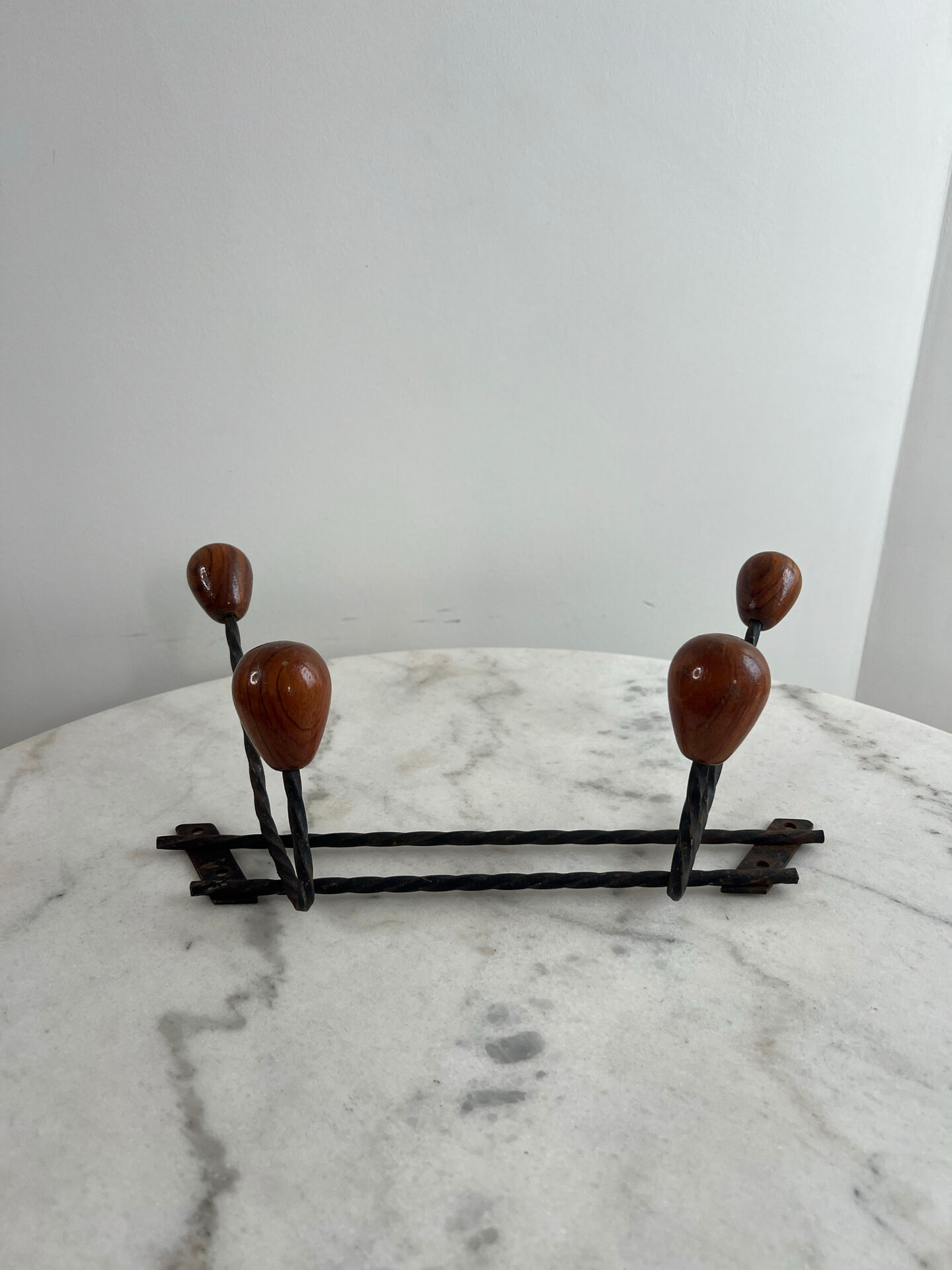 Wall-mounted coat rack in wrought iron with turned wooden knobs.