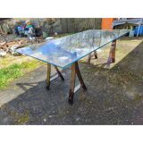 Vintage table with a glass top and smoked plastic trestle legs.