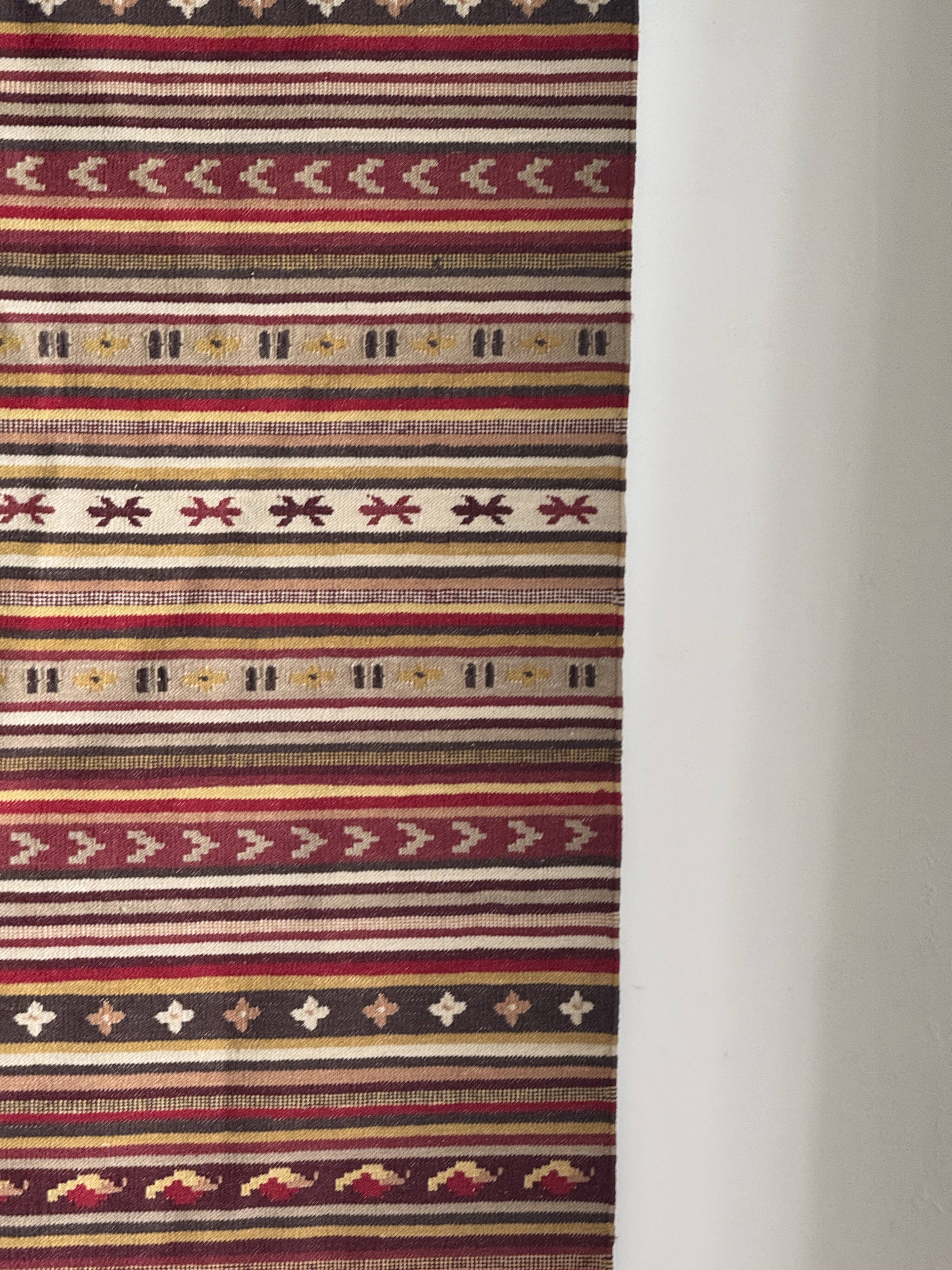 Large Indian rug with red, yellow, and white stripes and geometric fringes.