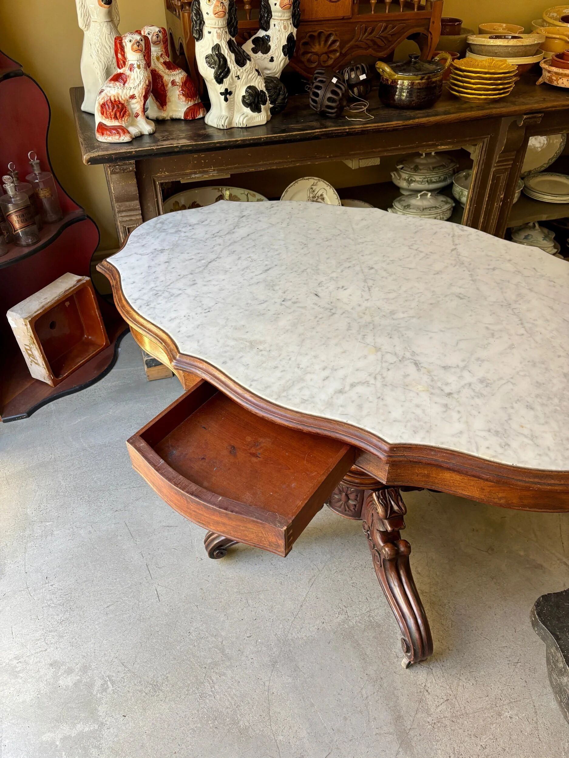 Table with a carved wooden frame and grey marble top on wheels, measuring 130 x 82 cm.