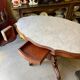 Table with a carved wooden frame and grey marble top on wheels, measuring 130 x 82 cm.
