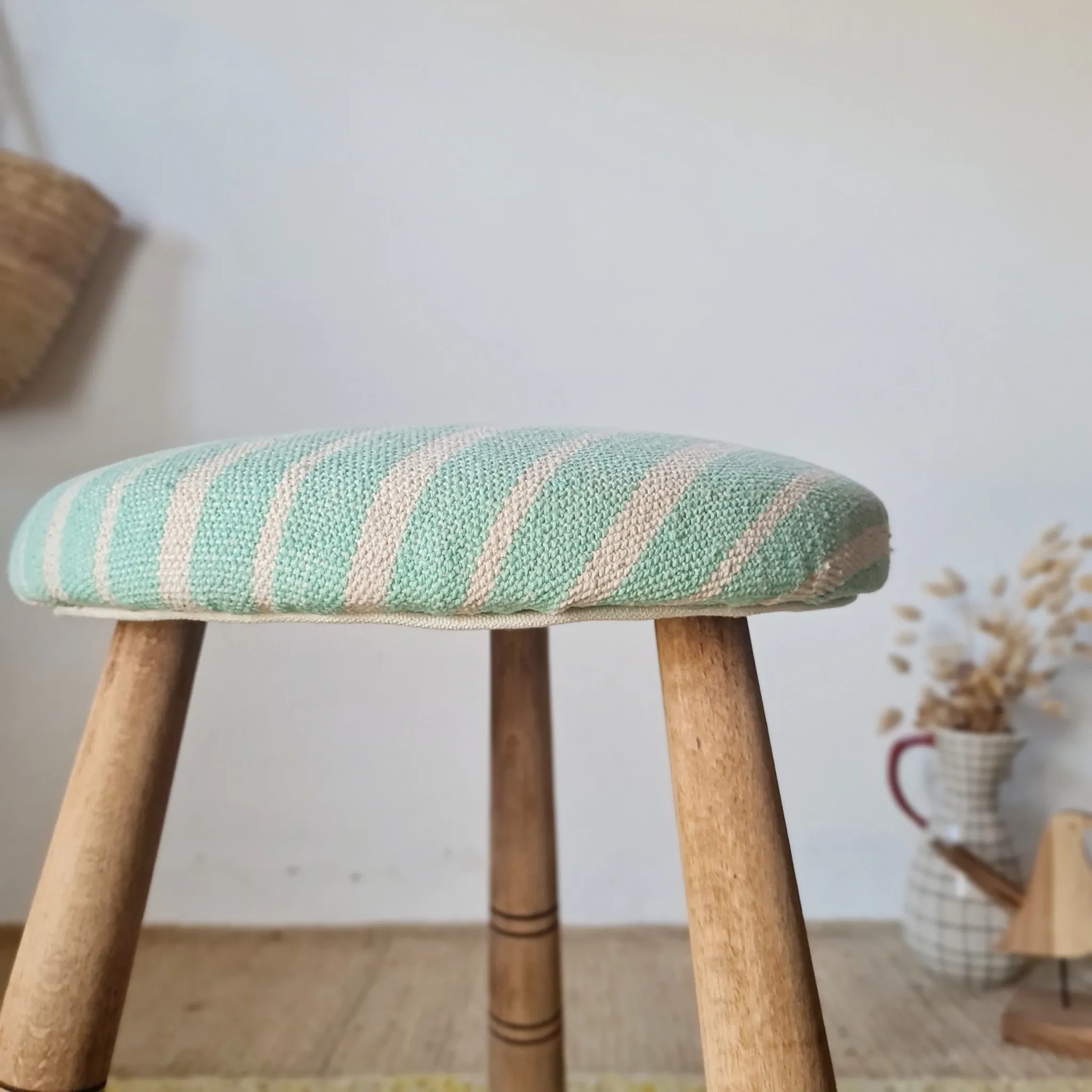 Antique tripod stool with blue striped seat.