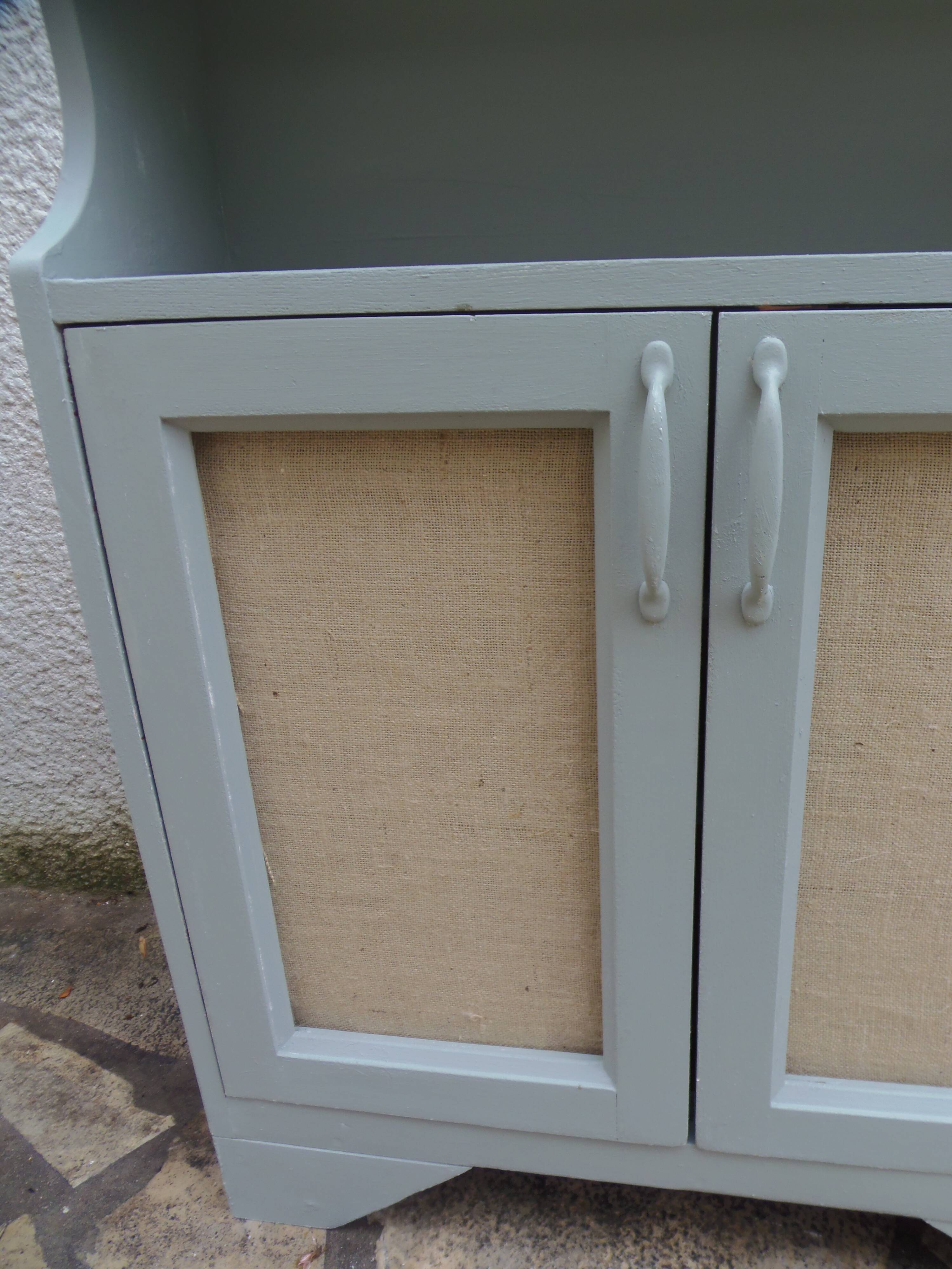 Small vintage green-grey piece of furniture, with 2 doors covered in burlap.