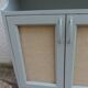 Small vintage green-grey piece of furniture, with 2 doors covered in burlap.