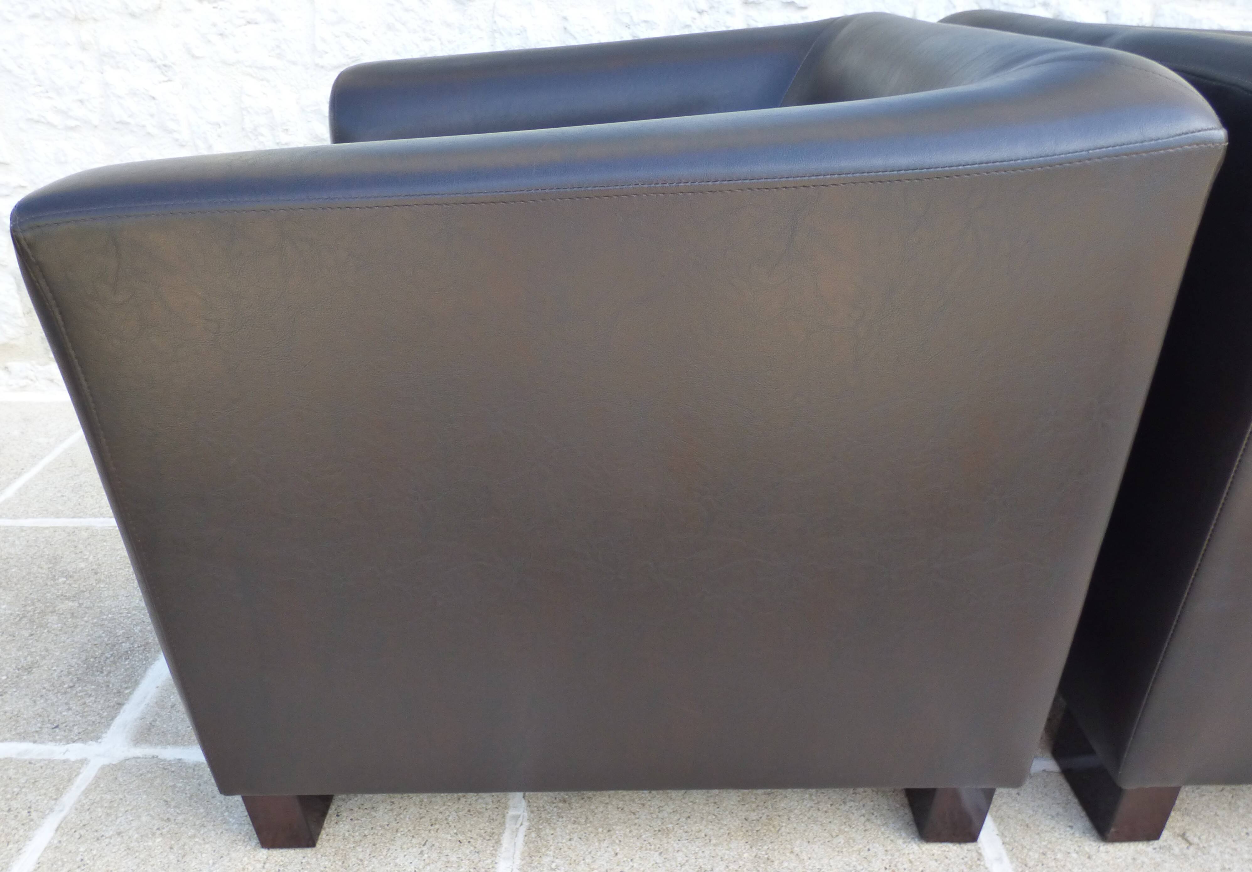 2 club armchairs with a chocolate faux leather seat and backrest and wooden legs.