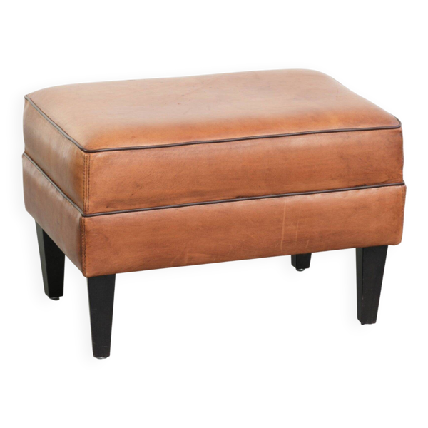 Pouf en peau de mouton pratique avec des couleurs chaudes, fini avec un passepoil noir.