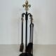 Neoclassical-style fire accessory in black lacquered metal and brass with fleur-de-lis.