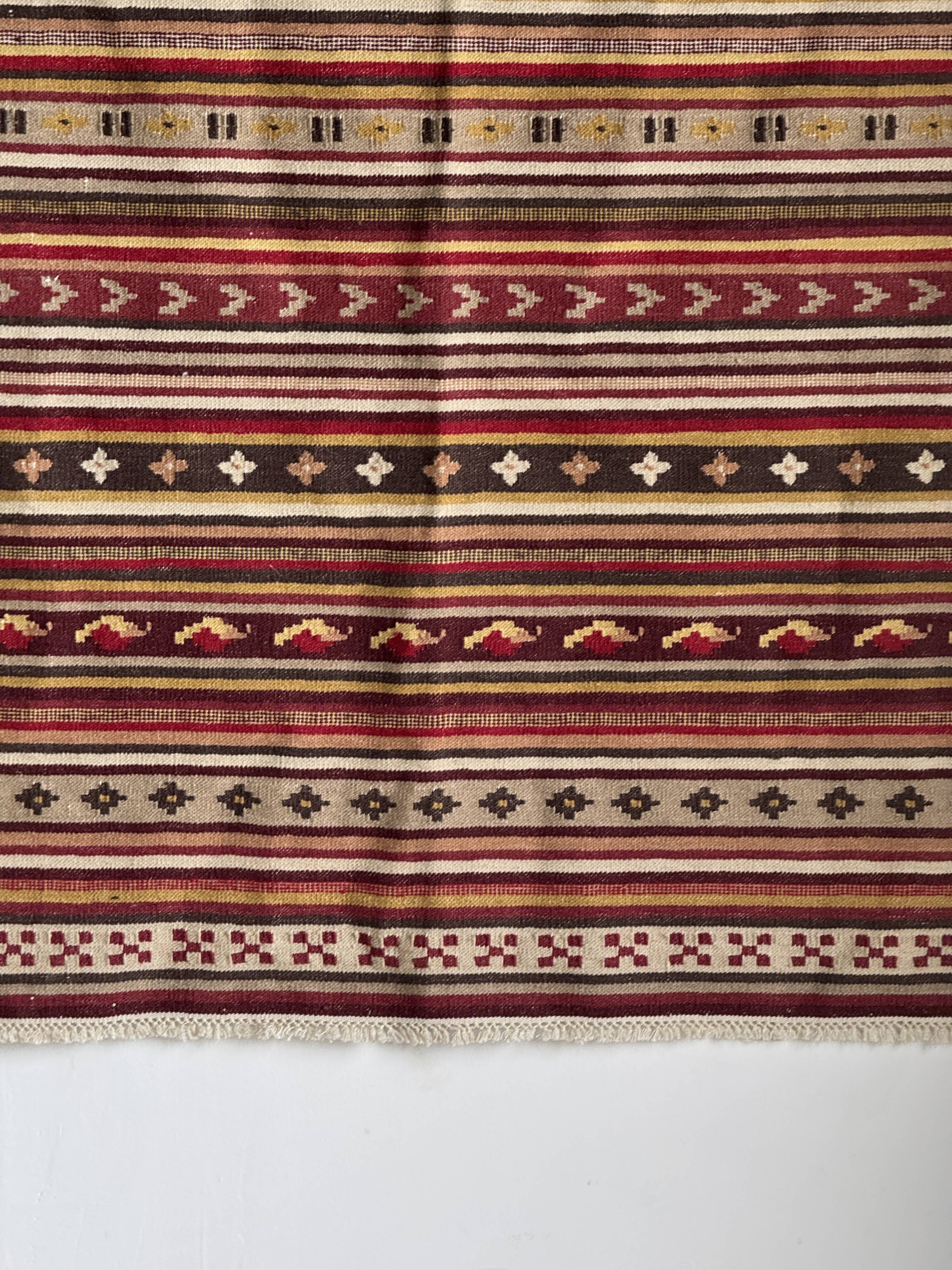 Large Indian rug with red, yellow, and white stripes and geometric fringes.
