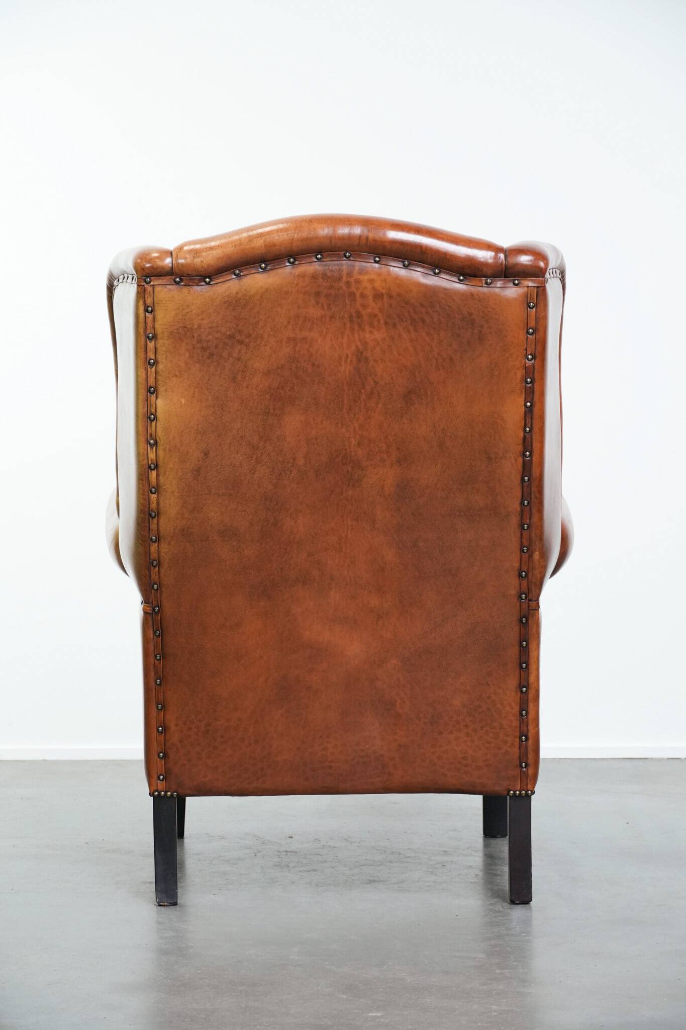 Large sheepskin wingback chair with black piping and decorative nails