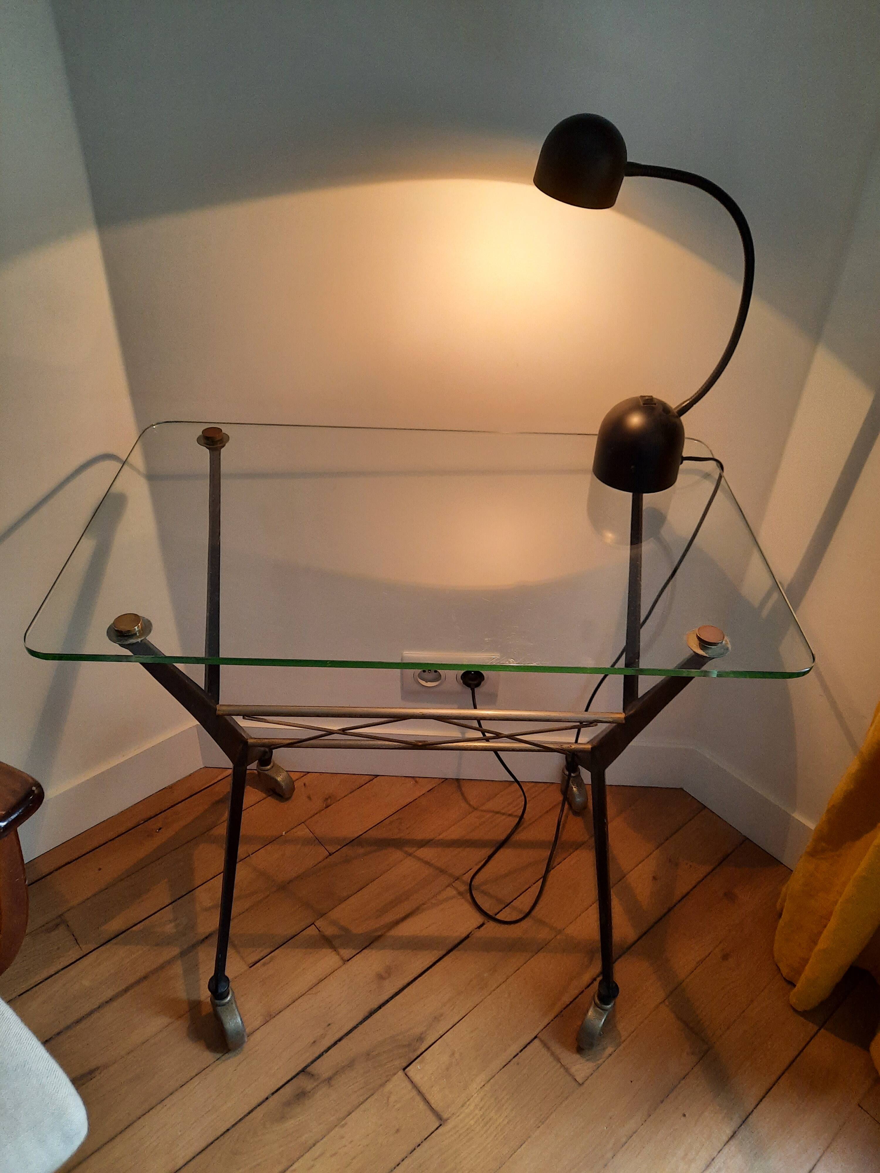 Vintage table with thick glass top and black steel legs with casters.