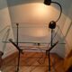 Vintage table with thick glass top and black steel legs with casters.