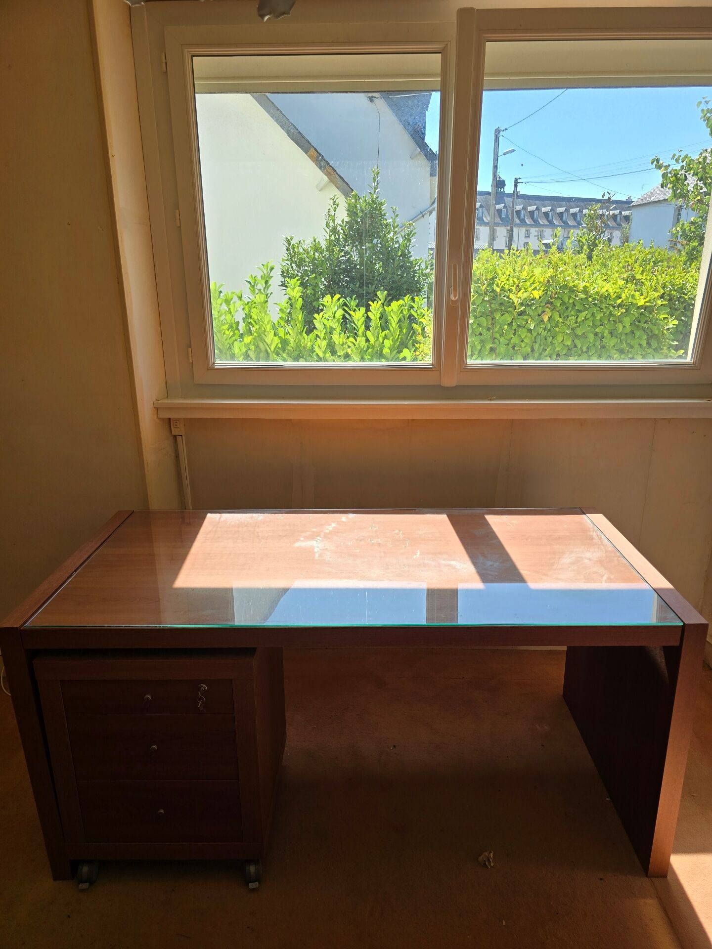 Large wooden desk with a glass top and a wheeled drawer unit.