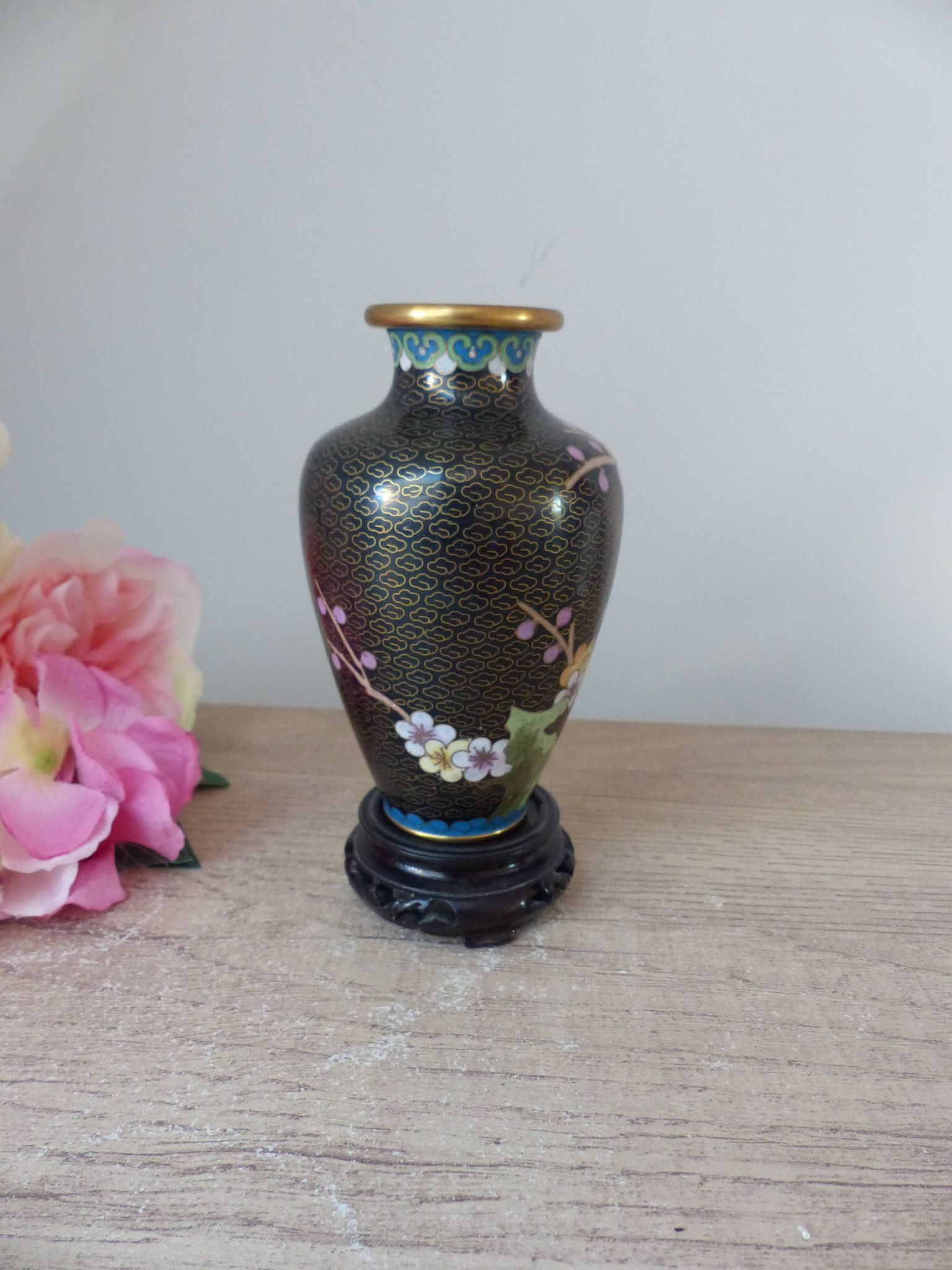 Small black cloisonné vase decorated with yellow and pink cherry blossoms, vase on wooden base
