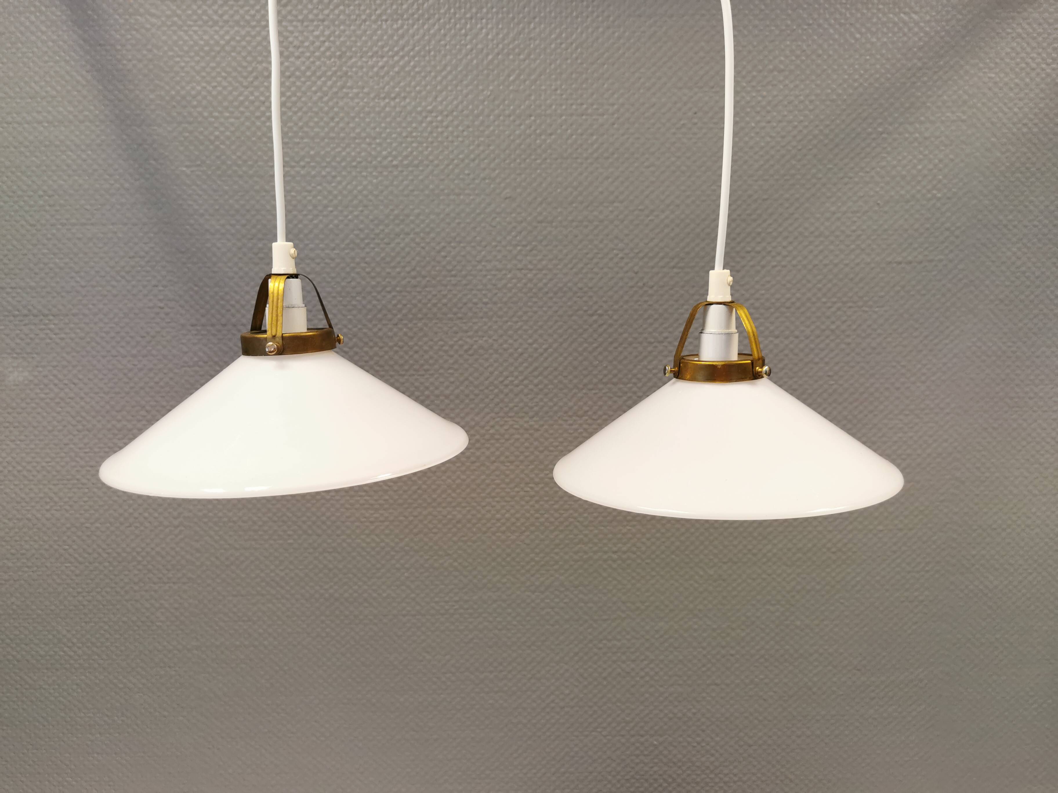 A set of hanging lamps in milky white opal glass with brass top.