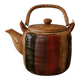 Vintage ceramic teapot with an enamel finish, rattan handle, warm tones.