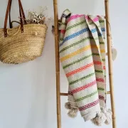 Moroccan plaid made of handwoven wool, decorated with stripes and pom-poms.
