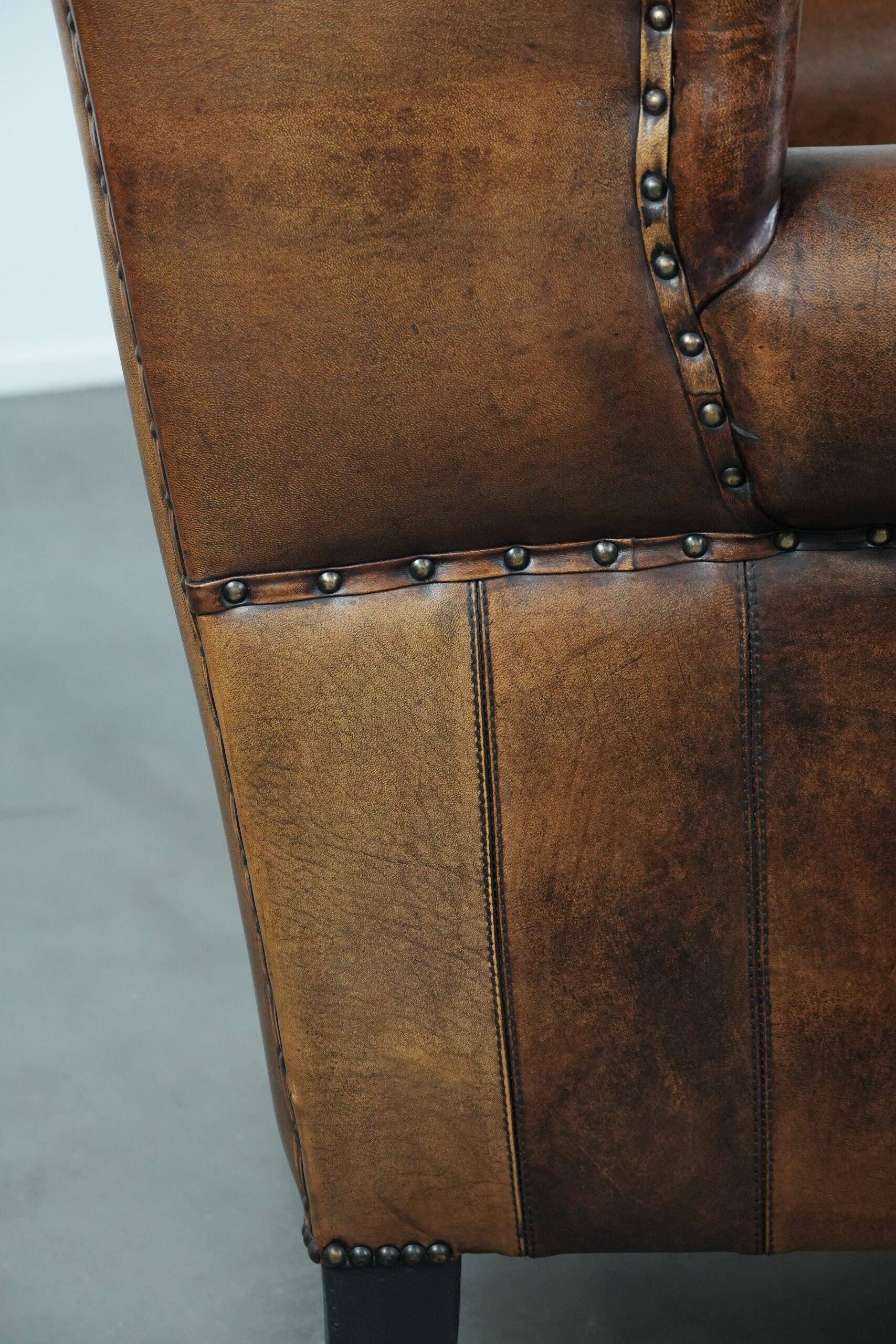 Sheepskin wingback armchair with decorative nails and black piping