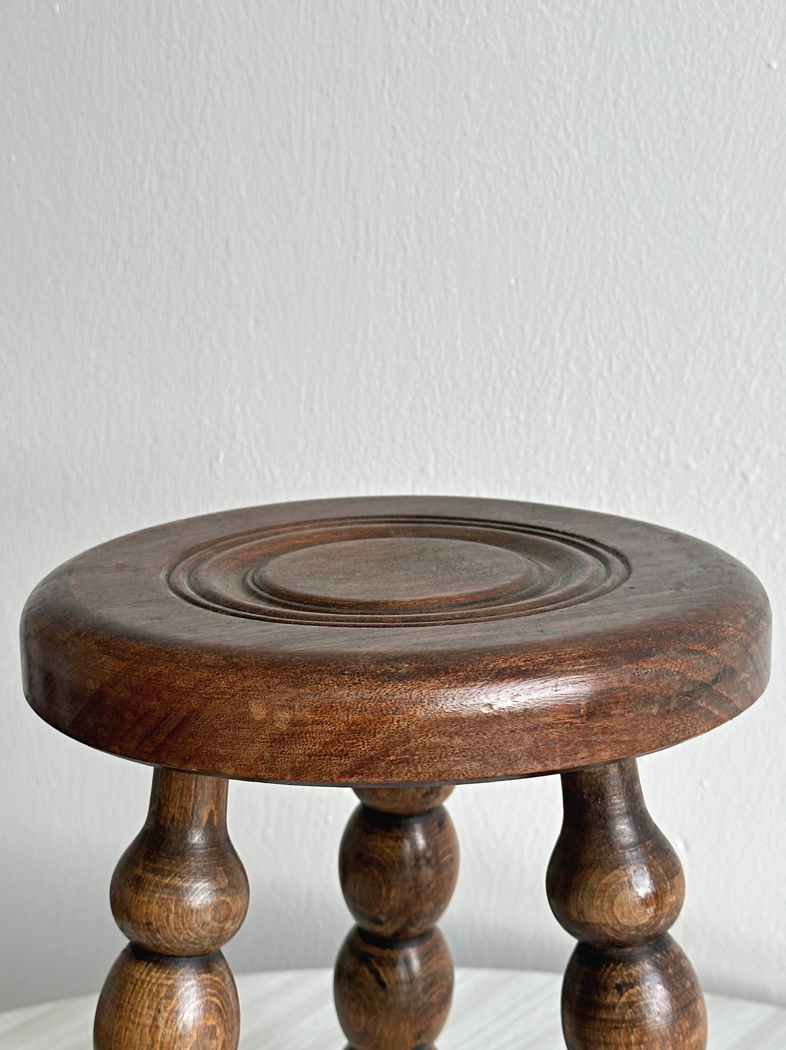 Small three-legged stool made of turned wood.