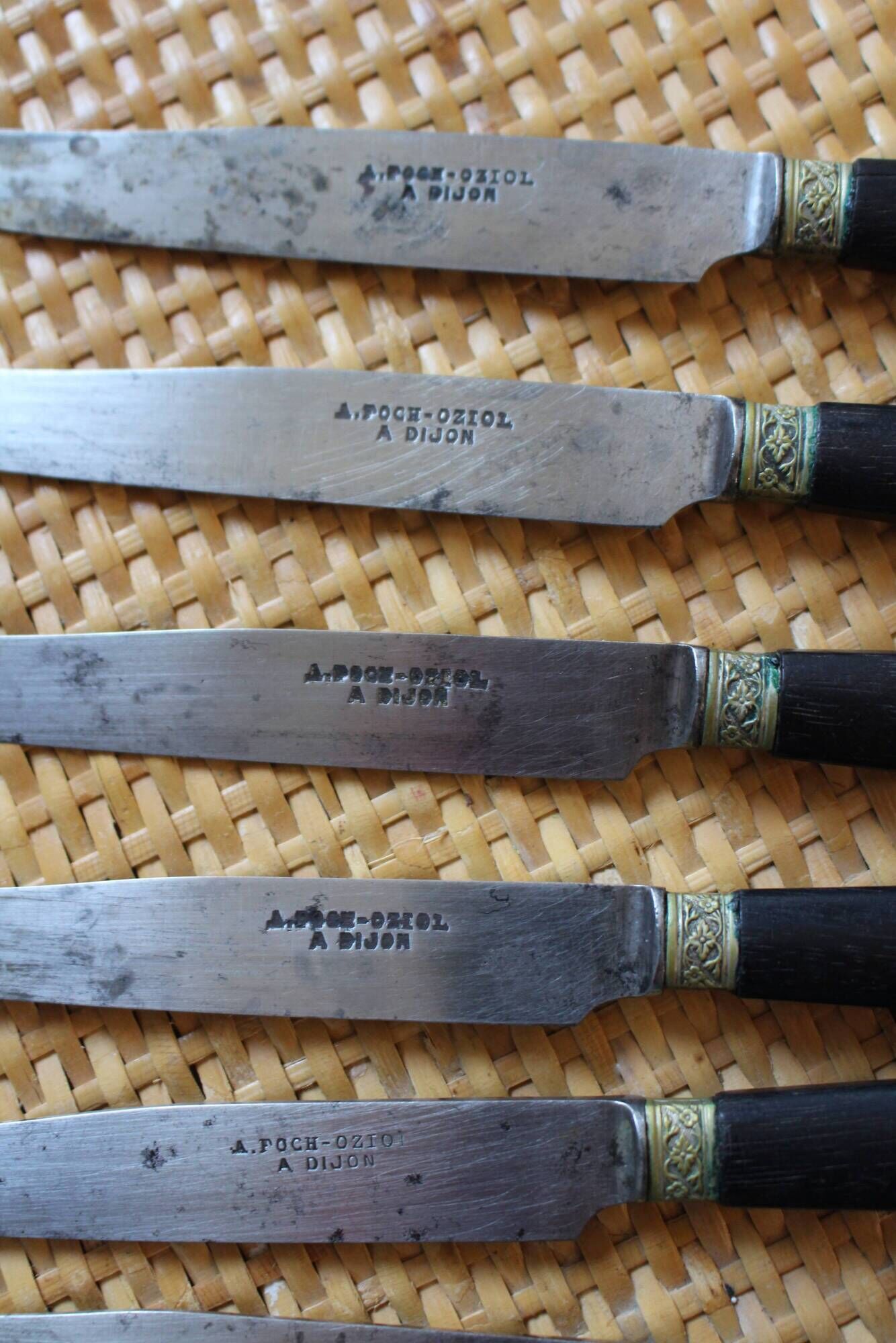 A set of 8 knives with black wooden handles and bolsters.