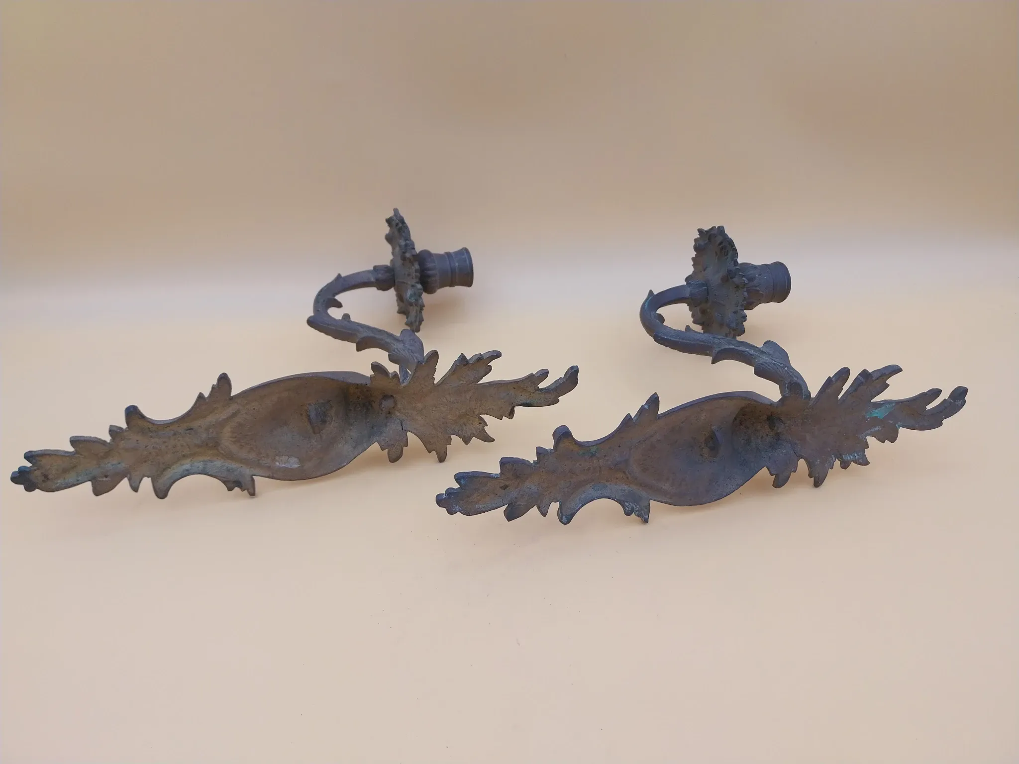 Pair of wall sconces in bronze candle holders with leaf medallion decoration.