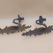 Pair of wall sconces in bronze candle holders with leaf medallion decoration.