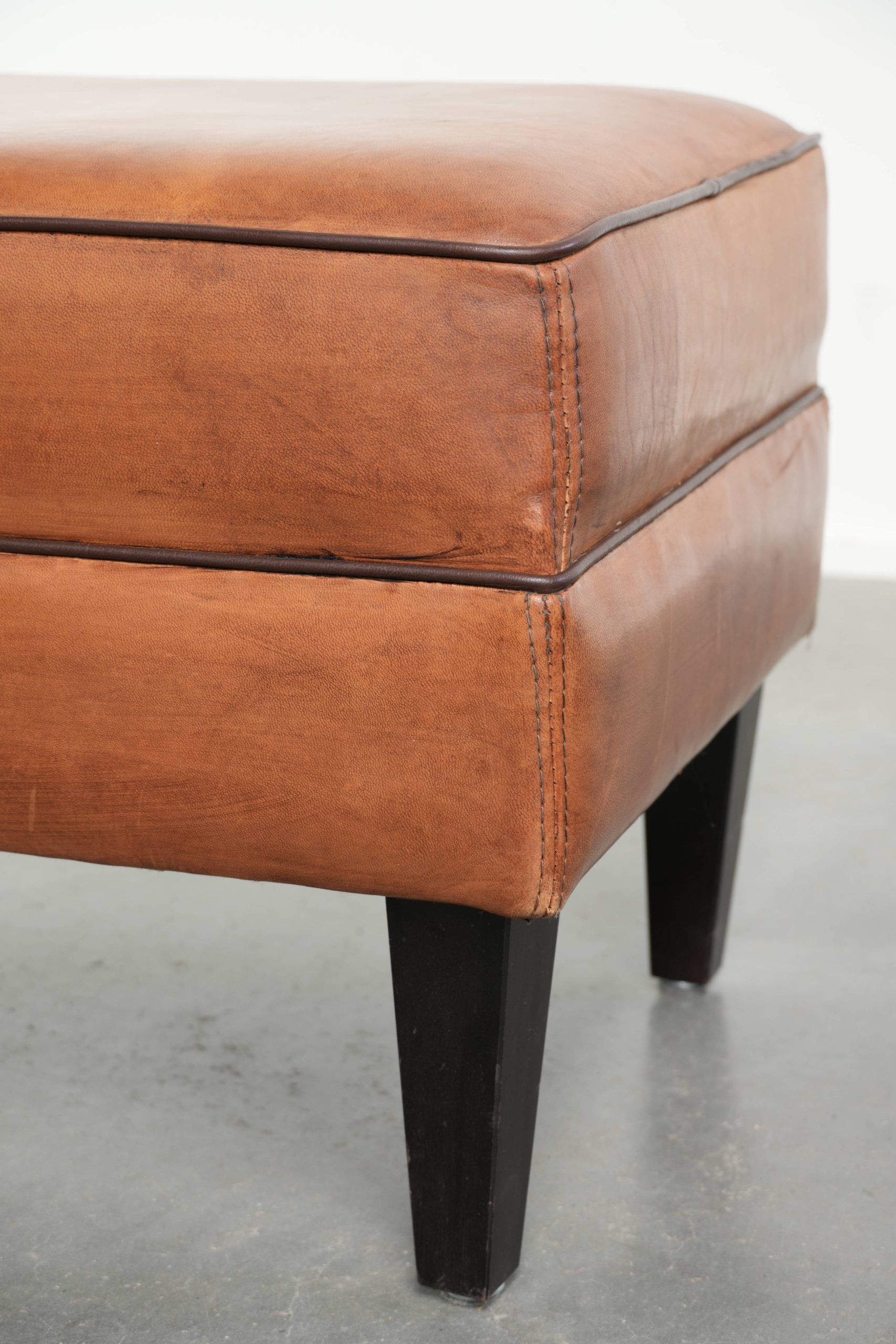 Handy sheepskin ottoman with warm colours finished with black piping