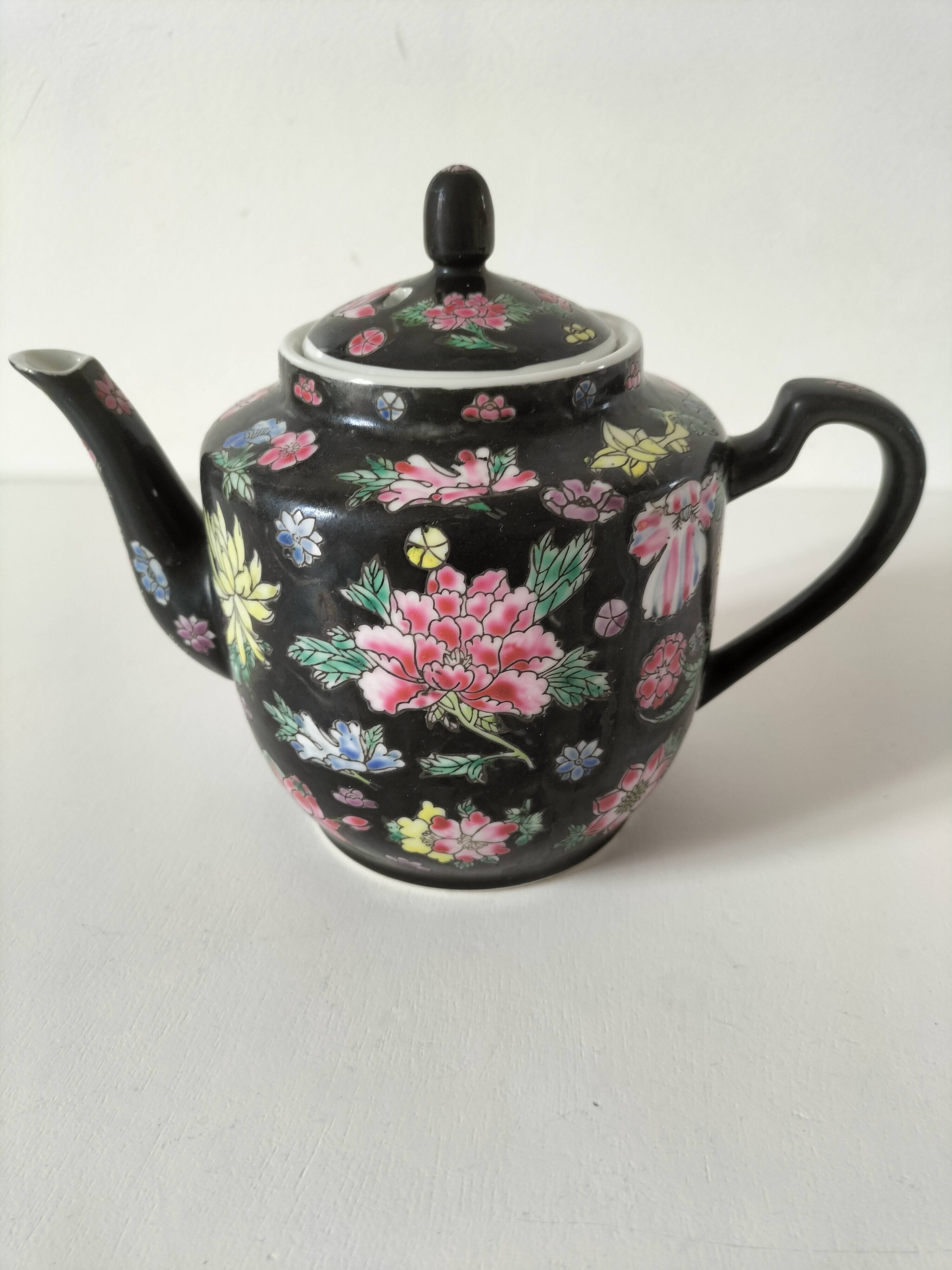 Vintage Chinese teapot with floral polychrome decoration on a black background.