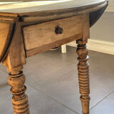 Oval wooden table with drop-leaf edges.