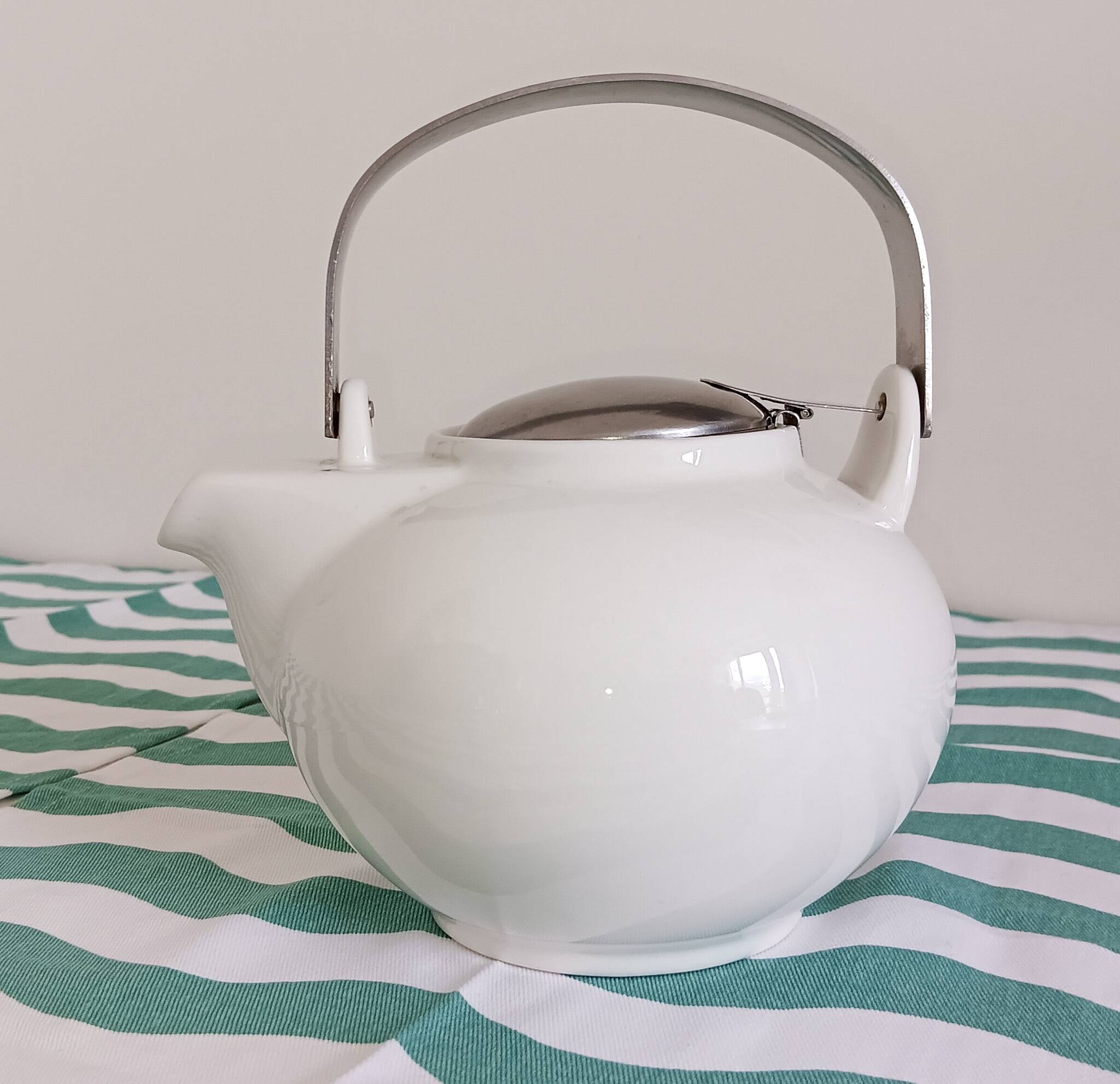 White porcelain teapot. Shiny stainless steel handle and lid
