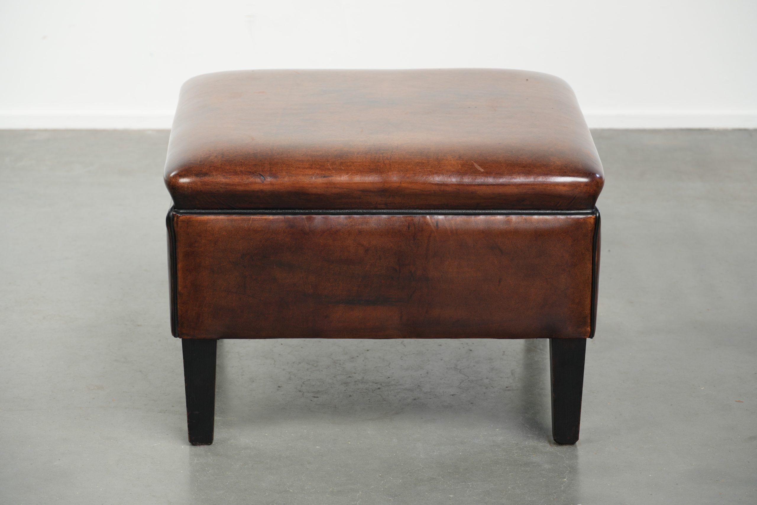 Large dark brown square ottoman made of sheepskin with black piping