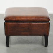 Pouf carré marron foncé en peau de mouton avec un passepoil noir.