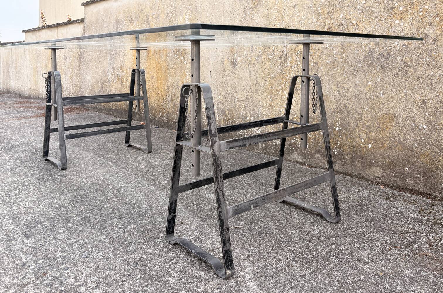 Large vintage industrial glass table with adjustable metal trestles.