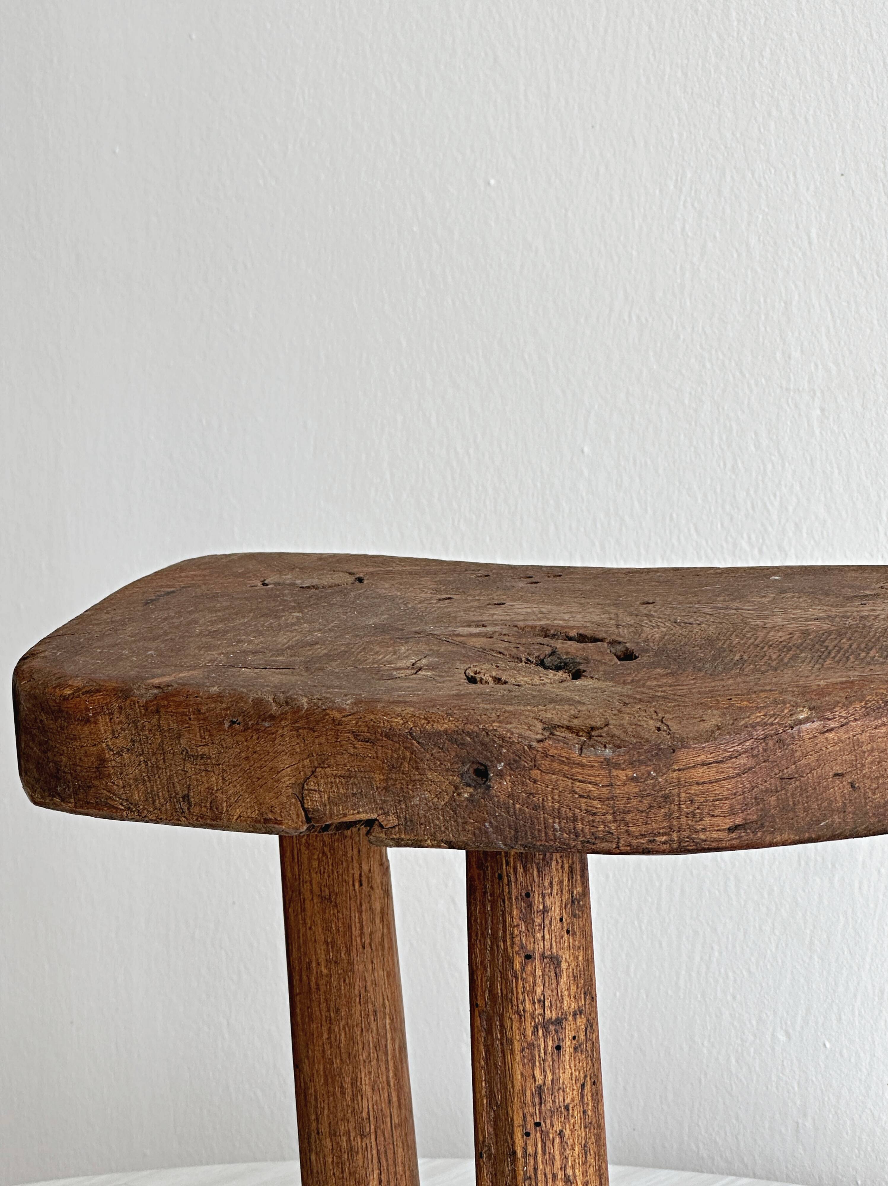Antique three-legged stool made of raw solid wood.
