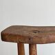 Antique three-legged stool made of raw solid wood.