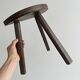 Antique wooden tripod stool with a semi-circular seat.