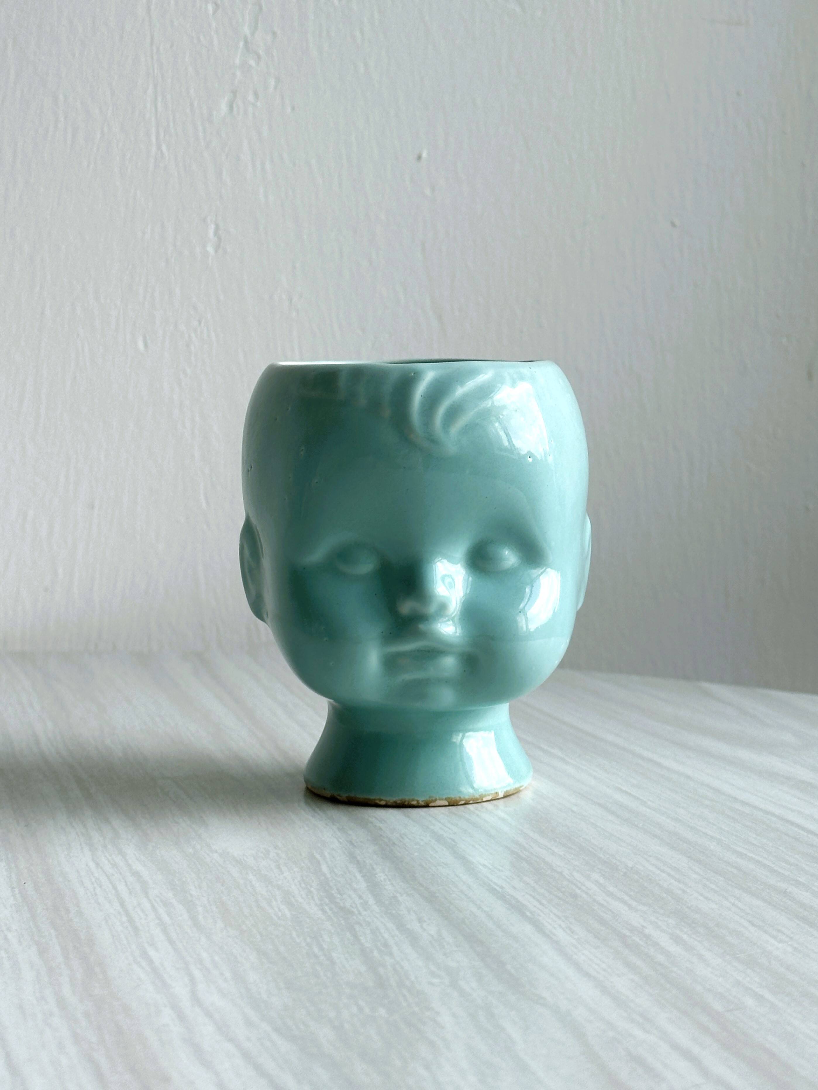 Turquoise plant pot in the shape of a vintage doll's head.