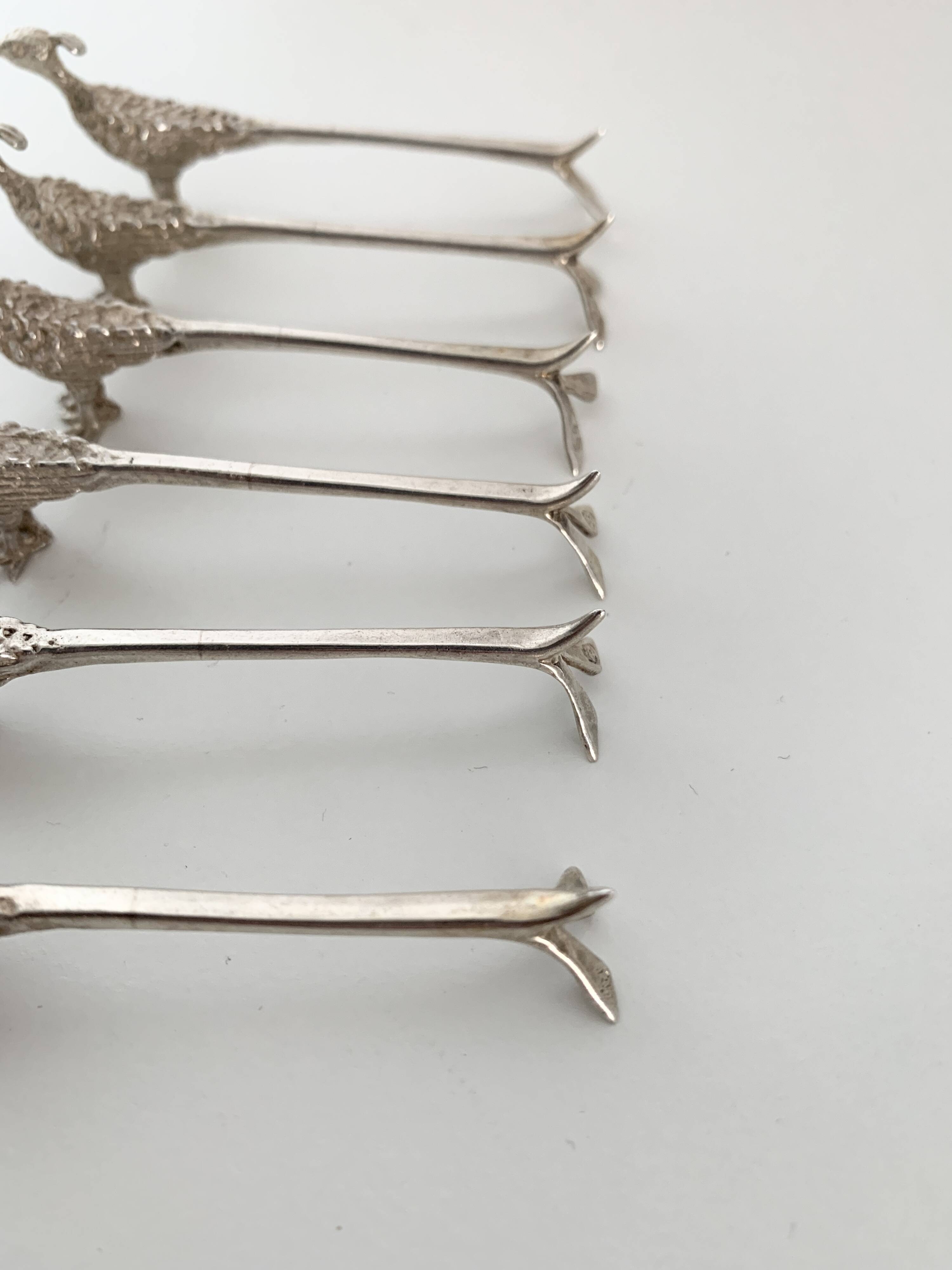 Six silver-plated knife rests in the shape of peacocks.