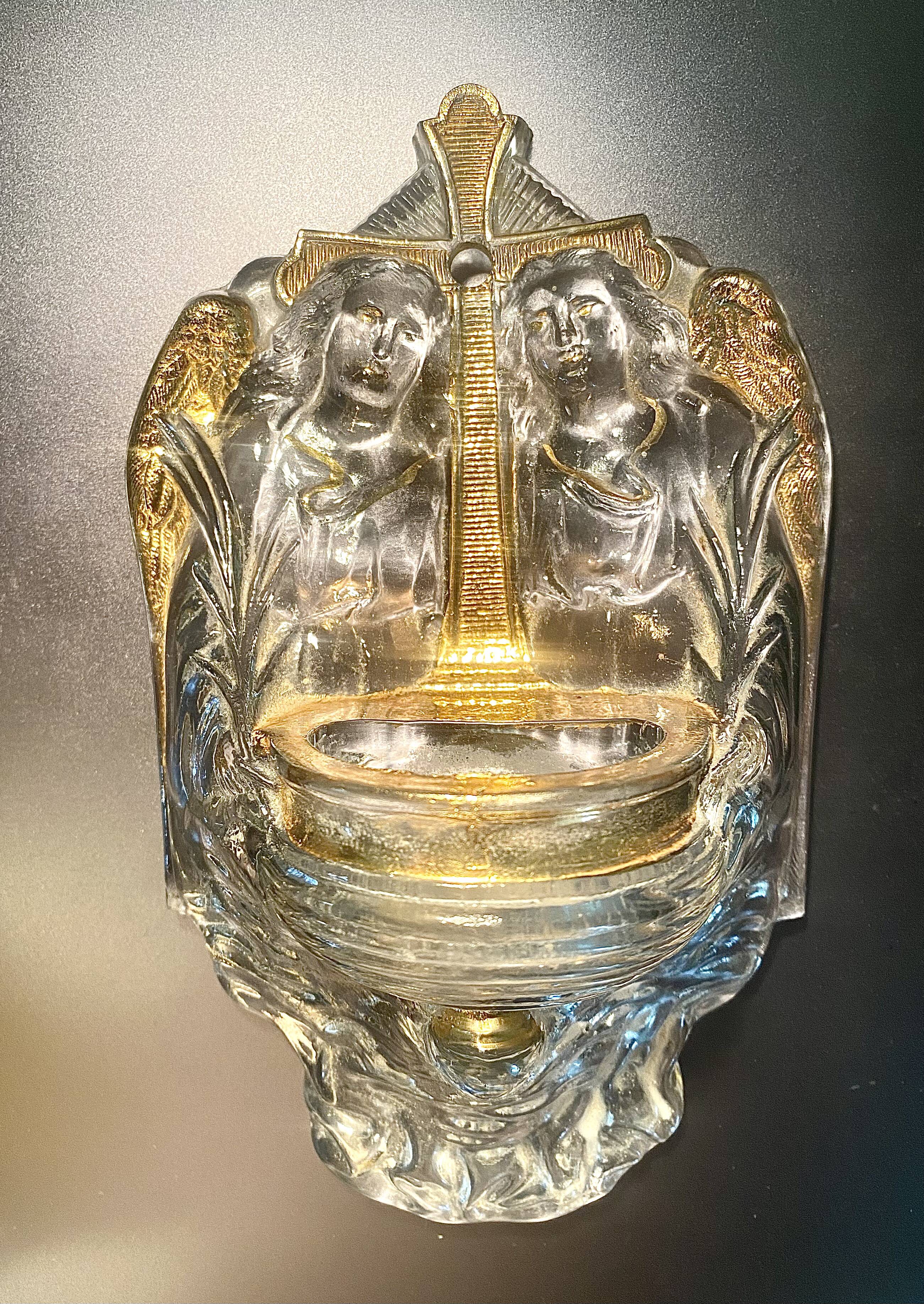 Old wall-mounted holy water font in moulded glass decorated with angels.