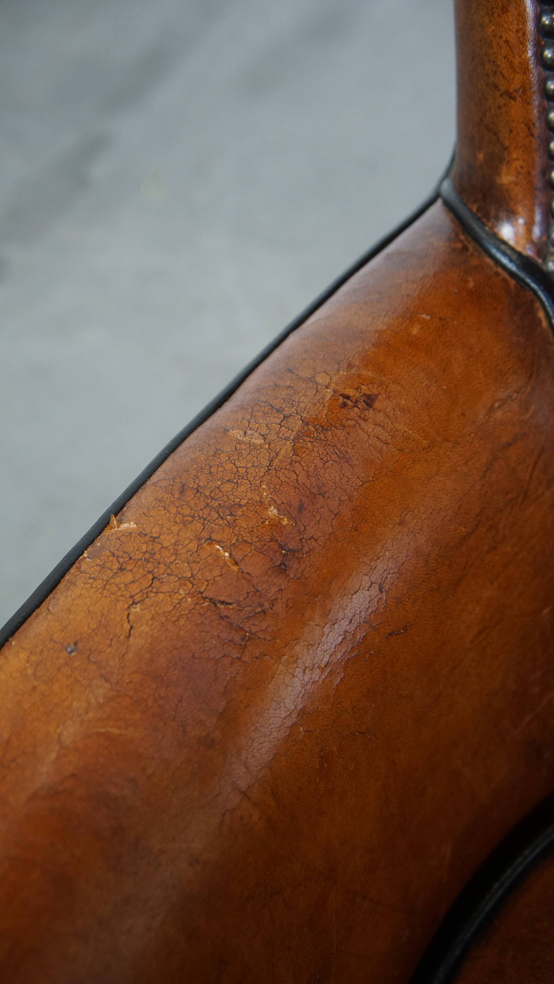 Cognac-colored sheepskin armchair with black piping and decorative nails