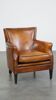 Cognac-colored sheepskin armchair with black piping and decorative nails