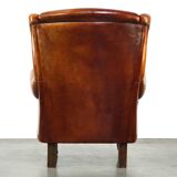 Subtle sheepskin wing chair in good condition on brass front wheels