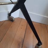 Vintage table with thick glass top and black steel legs with casters.