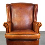 Subtle sheepskin wing chair in good condition on brass front wheels