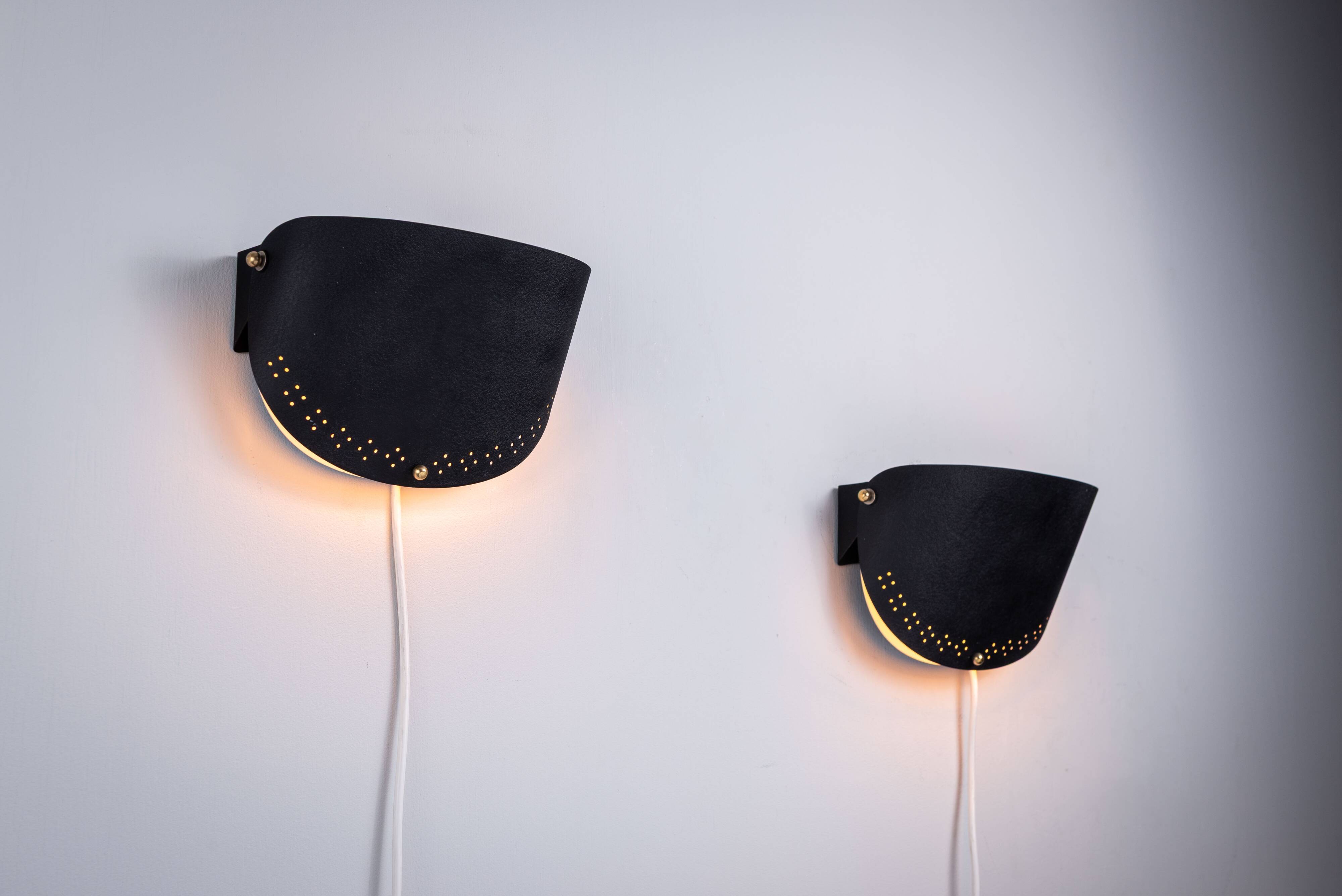 Matte black wall lamps with perforated shades and brass details