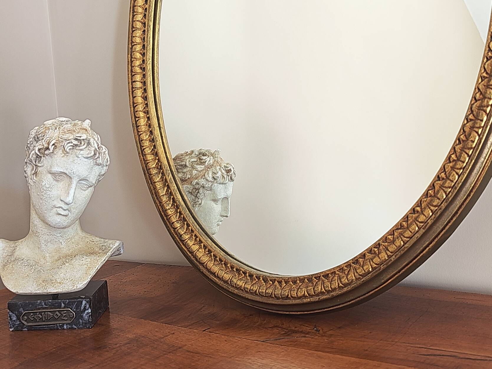 Vintage oval mirror with a carved wooden frame in gold, decorated with a bow.