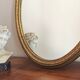 Vintage oval mirror with a carved wooden frame in gold, decorated with a bow.