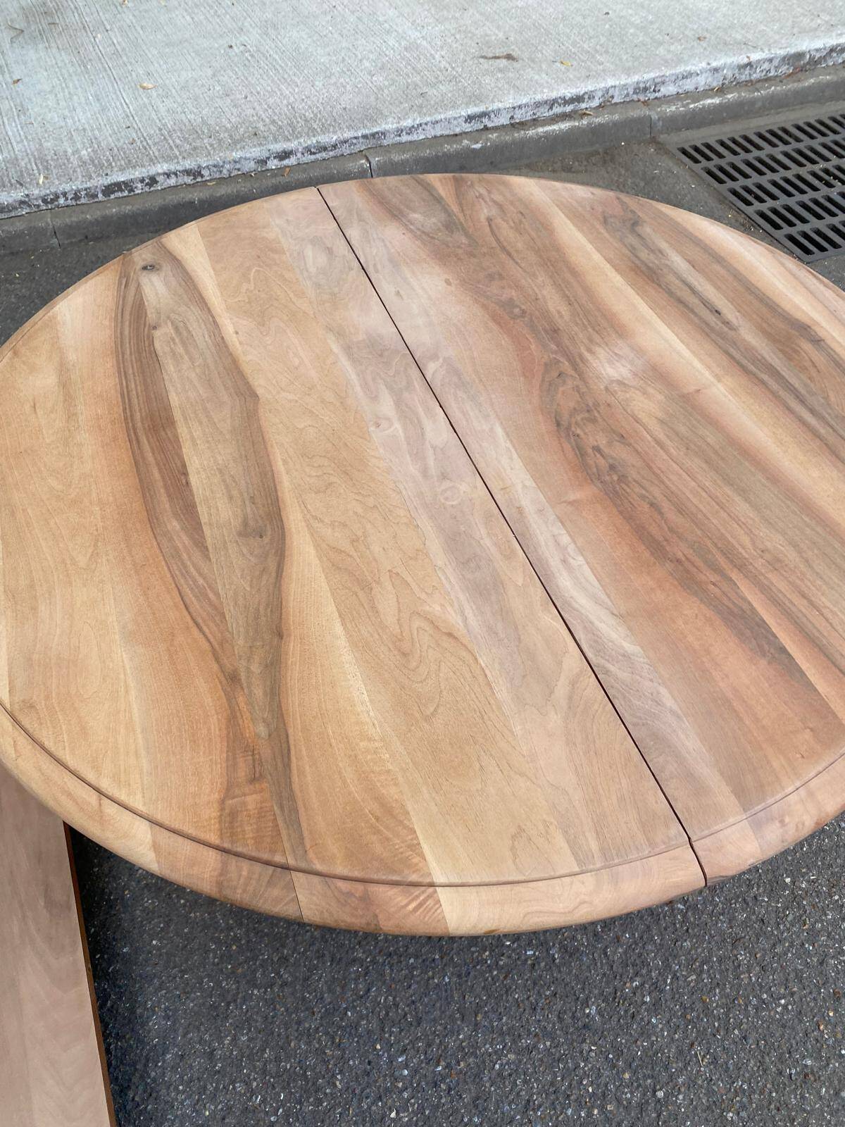 Round extendable dining table stripped in solid raw walnut with a central leg.