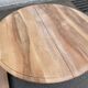Round extendable dining table stripped in solid raw walnut with a central leg.