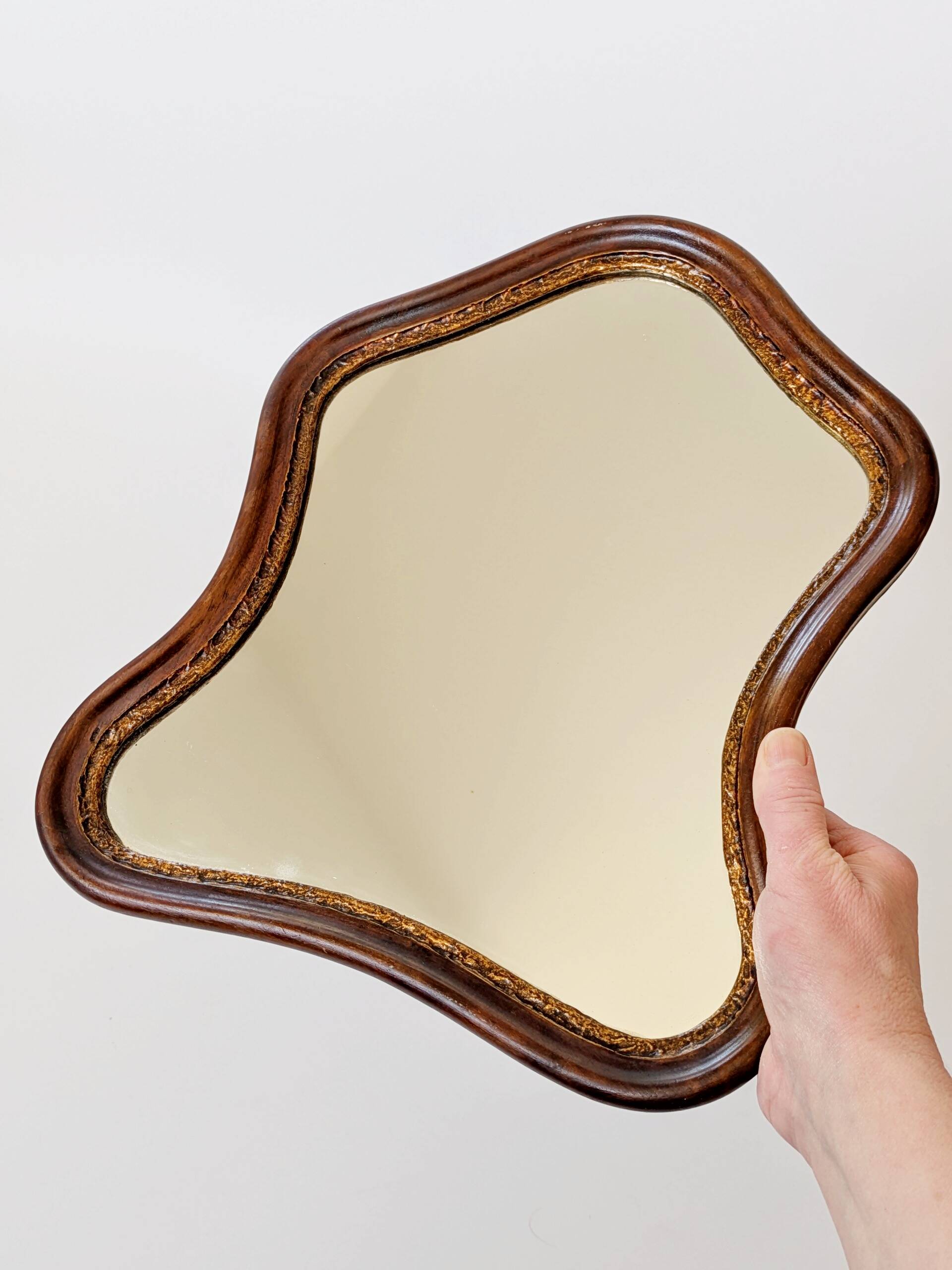 Antique wall mirror in carved wood with a wavy shape and a golden trim.