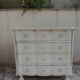A beautifully crafted crossbow-shaped chest of drawers, finished in pearl grey with a whitewashed top.